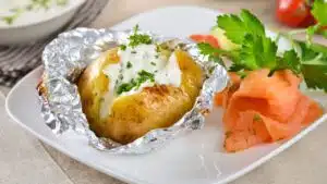 Wide image showing a baked potato on a white plate, with sour cream and chives.