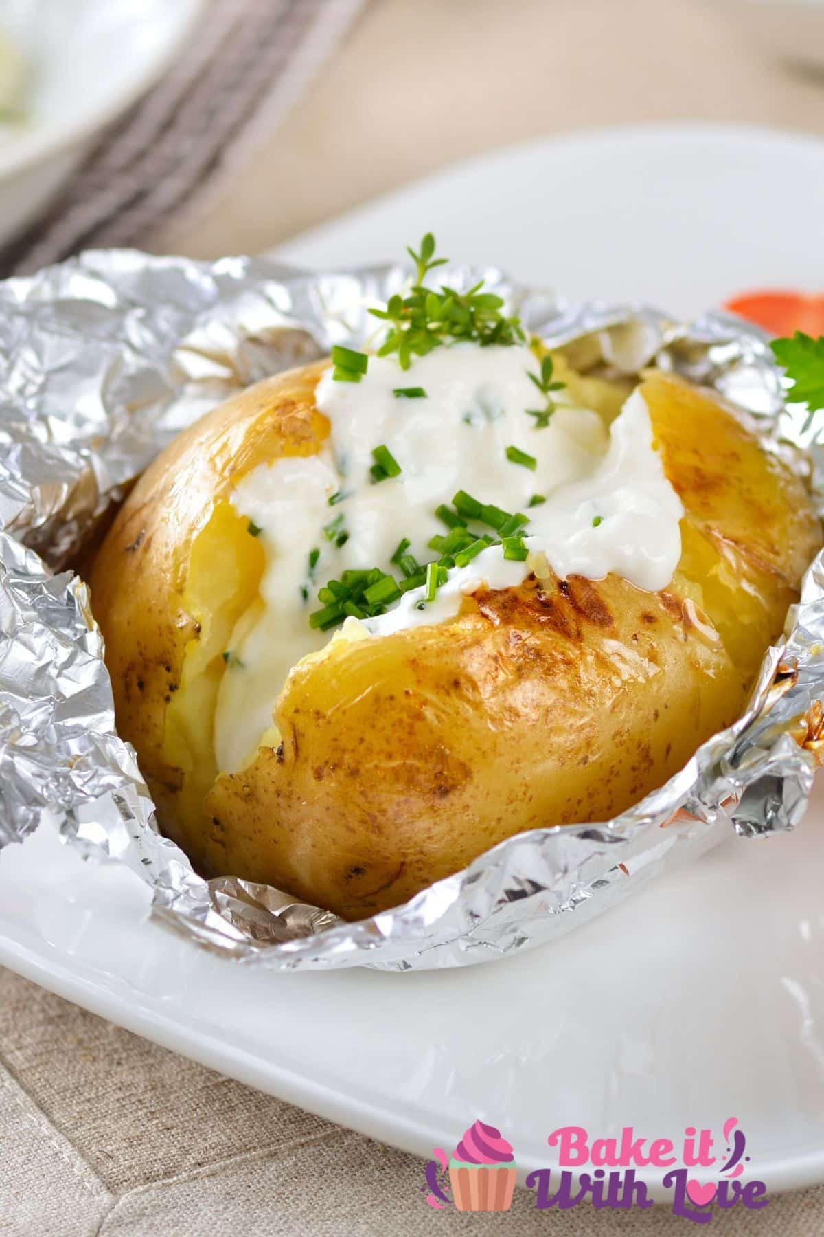 흰색 접시에 사워 크림과 골파를 곁들인 구운 감자를 보여주는 키가 큰 이미지.