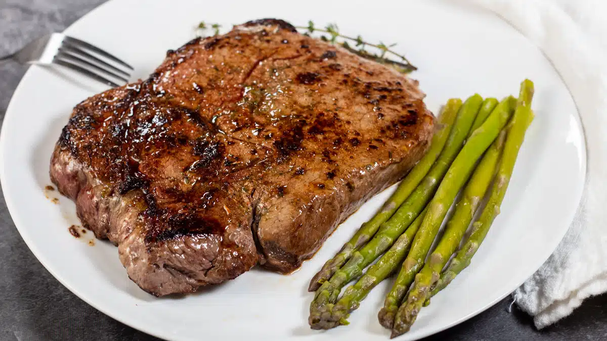 Wide image of a pan seared top sirloin steak on a white plate with asparagus.