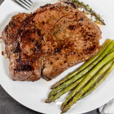 Square image of a pan seared top sirloin steak on a white plate with asparagus.