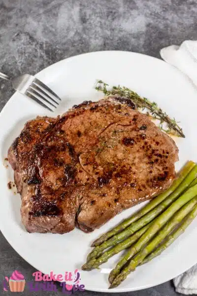 Tall image of a pan seared top sirloin steak on a white plate with asparagus.