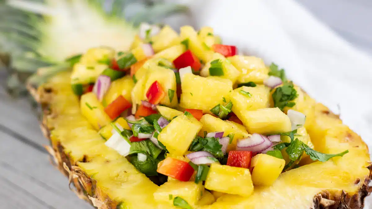 Wide image showing a cut in half pineapple filled with pineapple salsa.