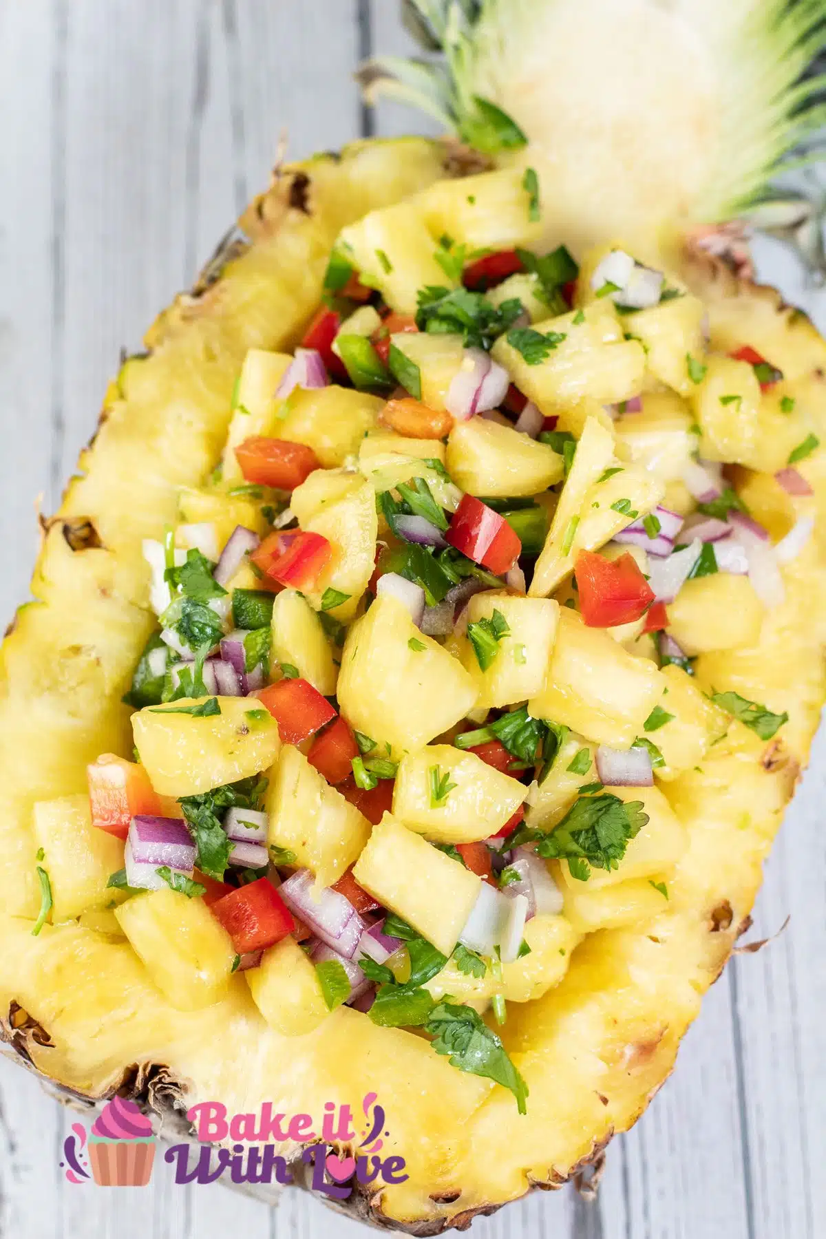 Tall image showing a cut in half pineapple filled with pineapple salsa.