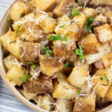 Wide image of slow cooker roasted potatoes in a bowl with a wooden spoon.