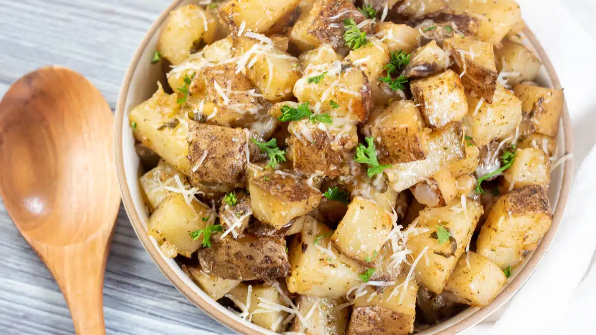 Wide image of slow cooker roasted potatoes in a bowl with a wooden spoon.