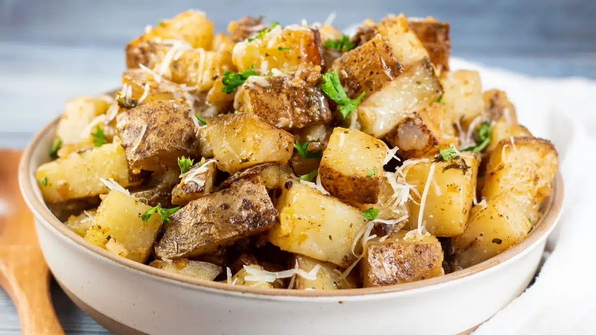 Wide close up image of slow cooker roasted potatoes in a bowl with a wooden spoon.