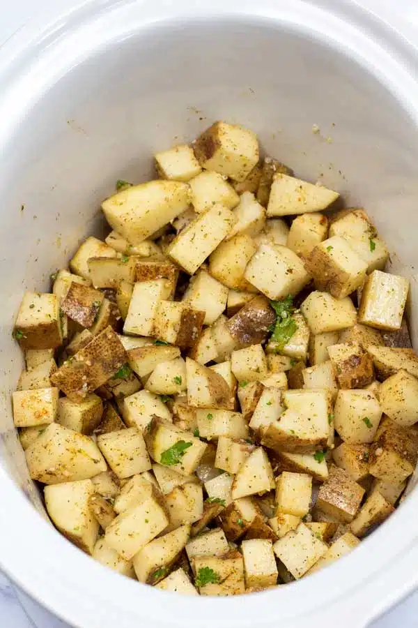 Process image 4 showing cubed potatoes in a crockpot tossed with seasoning.