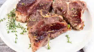 Wide image showing sous vide lamb chops on a white plate.
