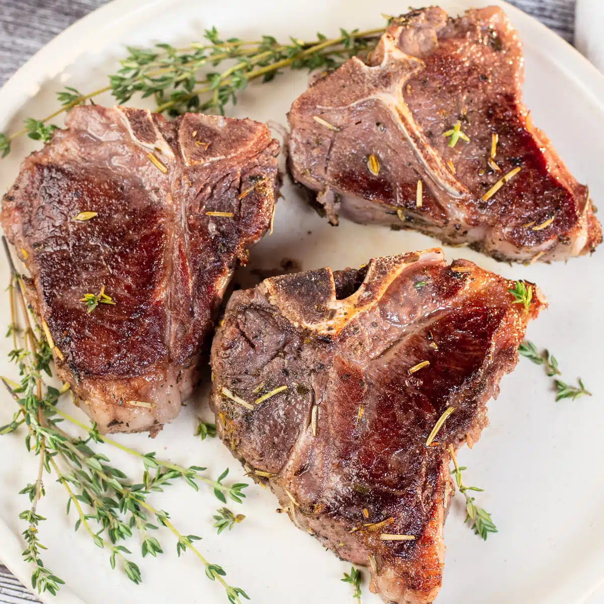 Square image showing sous vide lamb chops on a white plate.
