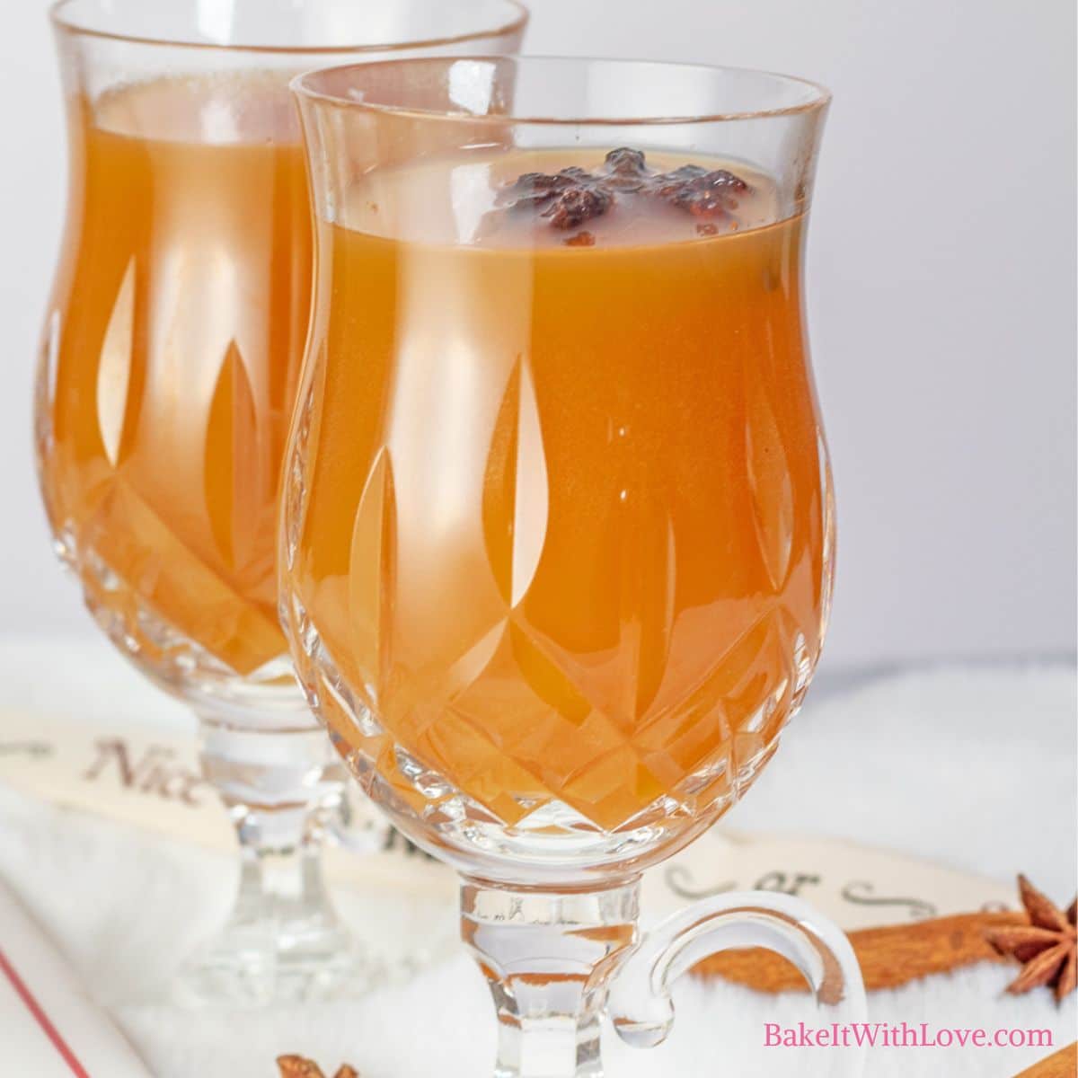 A square image showing two decorative glasses filled with homemade apple cider on white background.