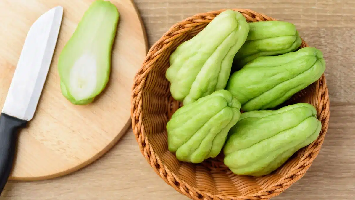 Chayote squash aka mirliton in a wicker basket and sliced open in a round wooden cutting board.