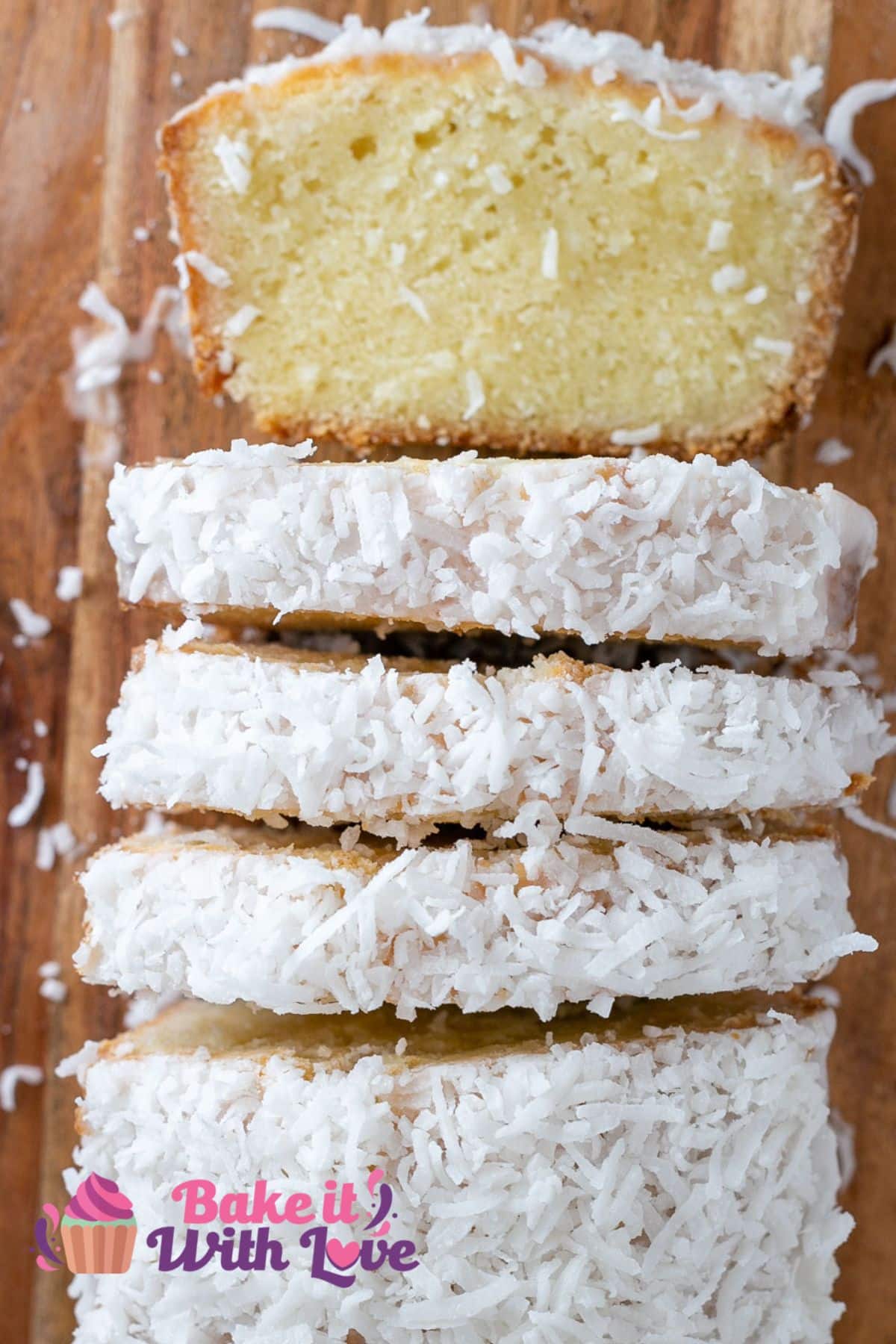 Coconut loaf cake overhead image with slices cut away and one laid down on wooden cutting board with scattered shredded sweetened coconut around the cake.