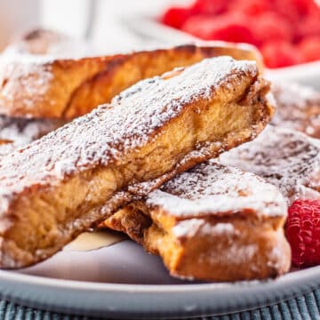 Tasty homemade French toast sticks on a white plate with berries around the stacked bread.