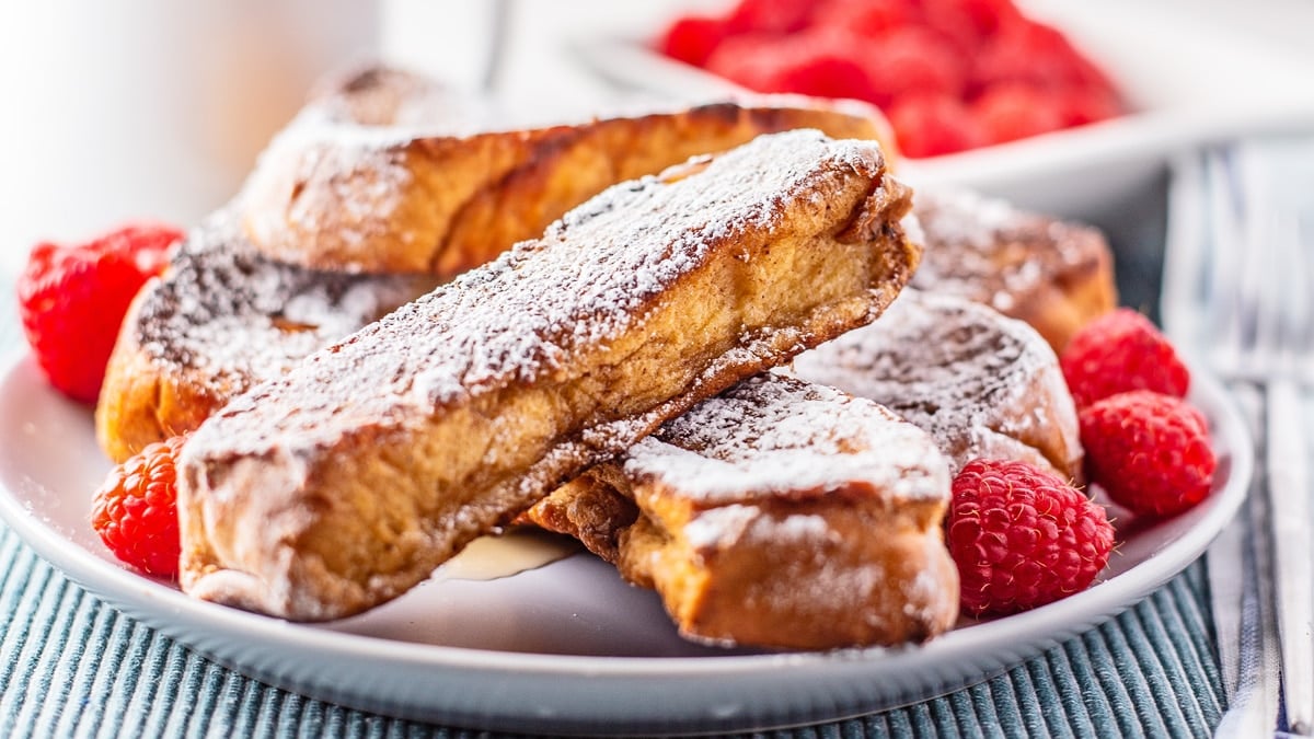 Tasty homemade French toast sticks on a white plate with berries around the stacked bread.