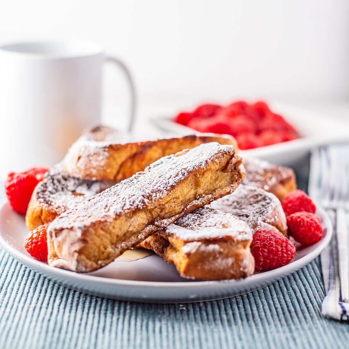 Best homemade French toast sticks recipe plated on a white plate, dusted with confectioners sugar, and served with fresh raspberries.
