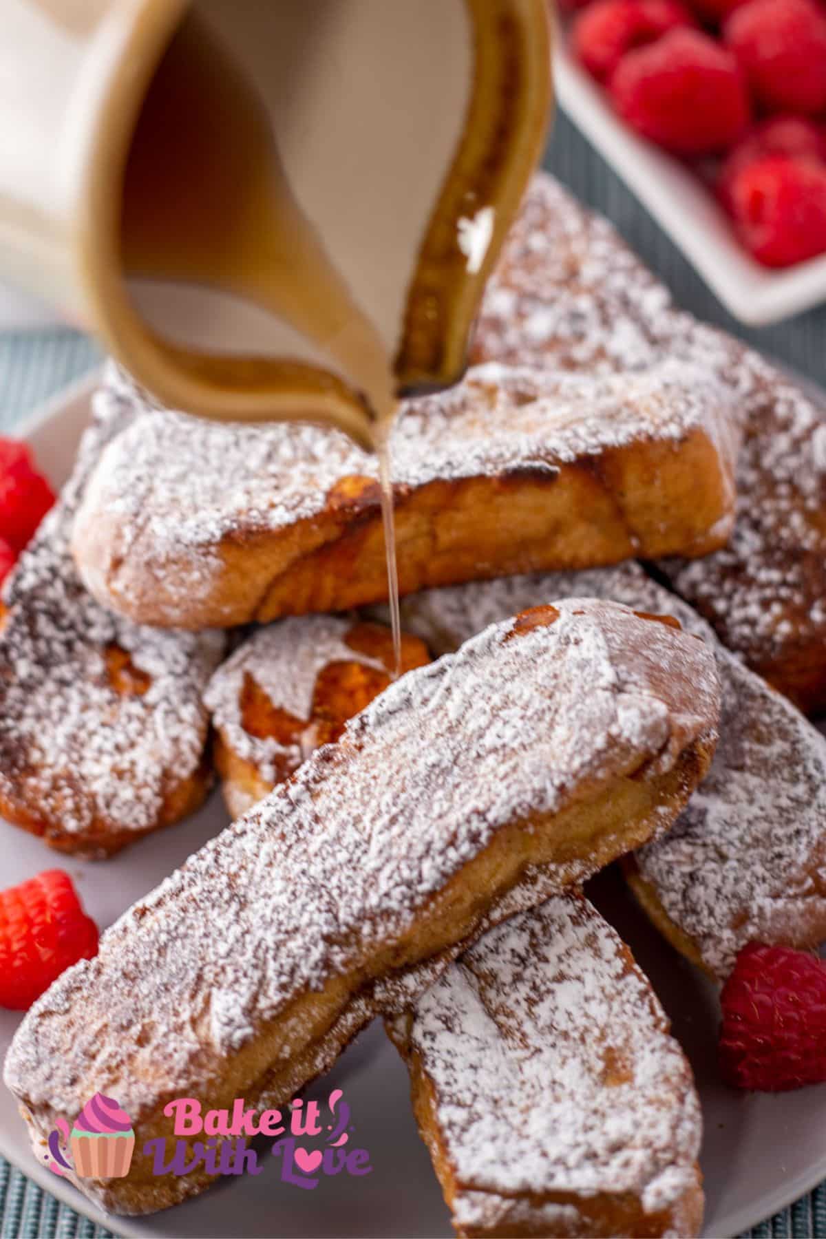 Tasty baked French toast sticks served on a plate dusted with confectioners sugar and maple syrup being poured over the stack.