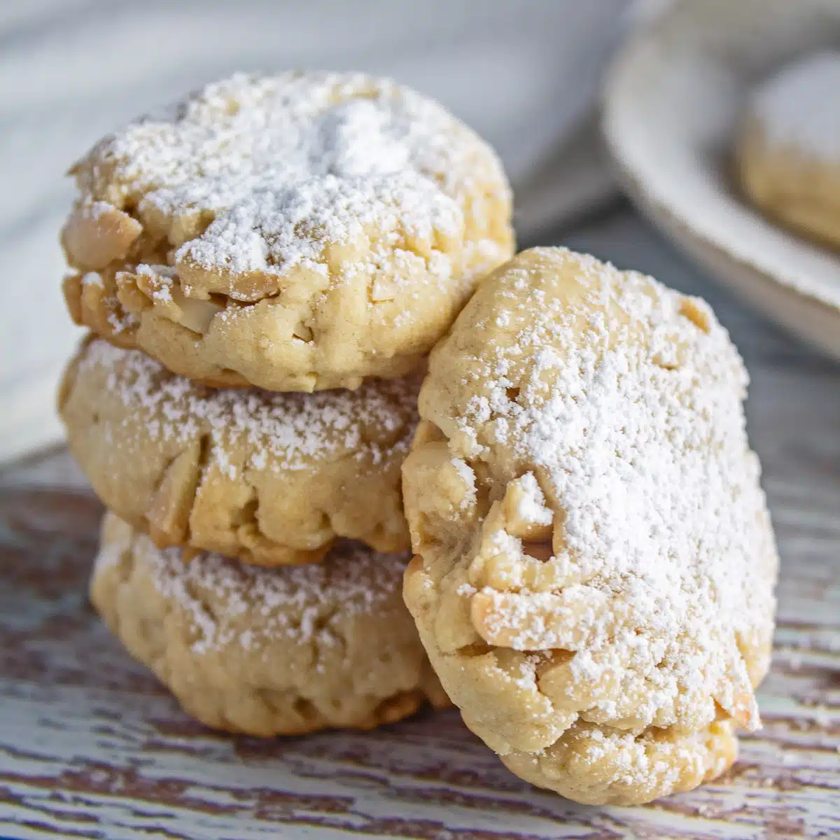 Best Greek almond cookies (kourabiedes) recipe with the tasty, crumbly textured cookies stacked three cookies high and a fourth cookie leaning against them.