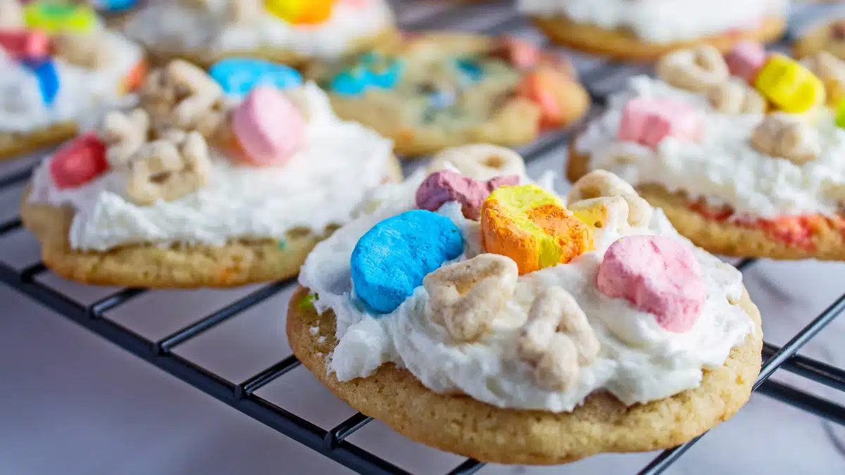 Lucky Charms cookies on wire cooling rack with the frosting just added and cereal topping.