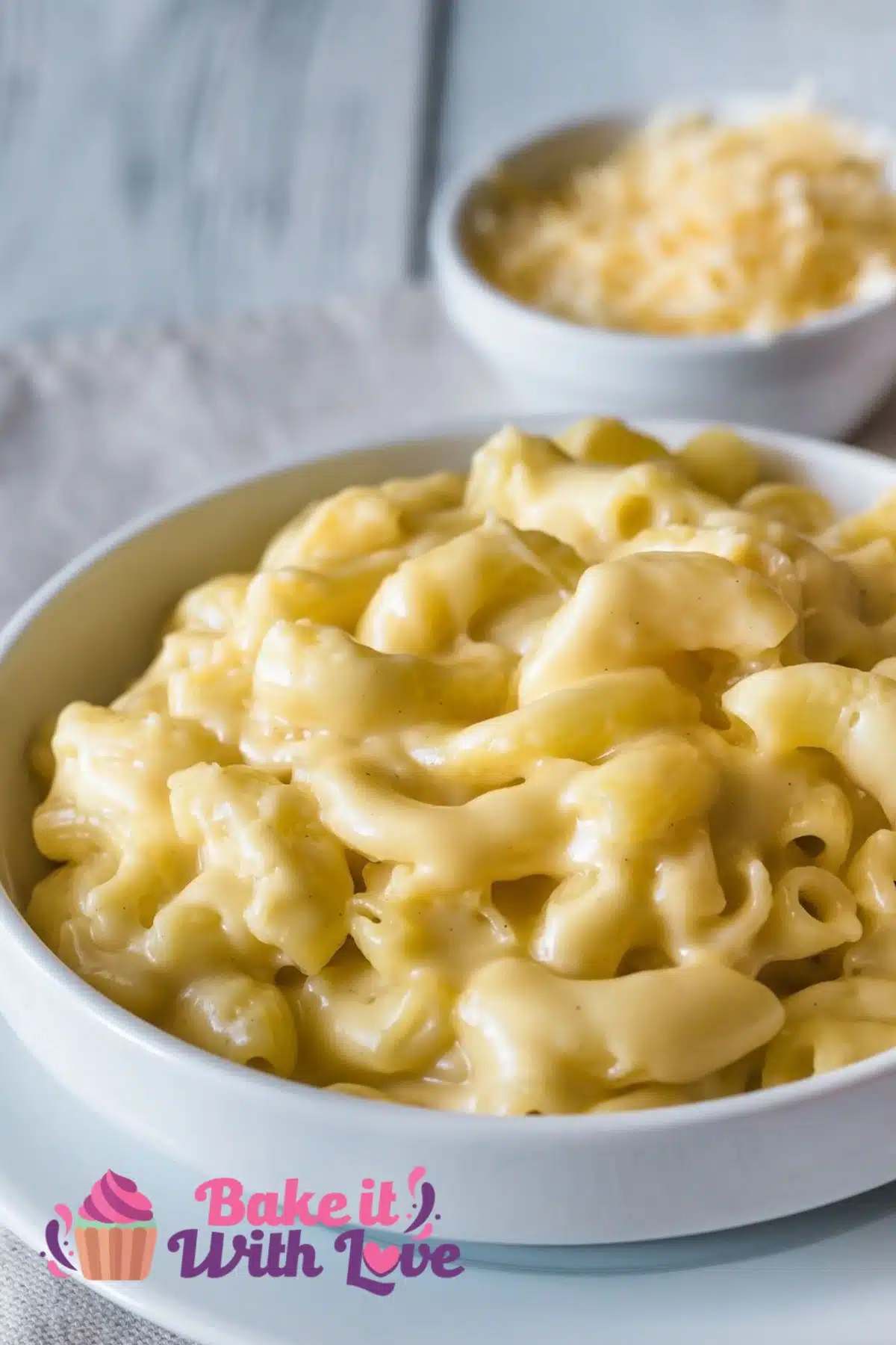 Creamy mac and cheese without flour served in a white bowl with a small bowl of grated cheddar cheese in the background.