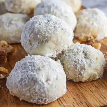 Best Mexican wedding cookies recipe bakes up tender and tasty like these cookies served on a cutting board with scattered walnuts.