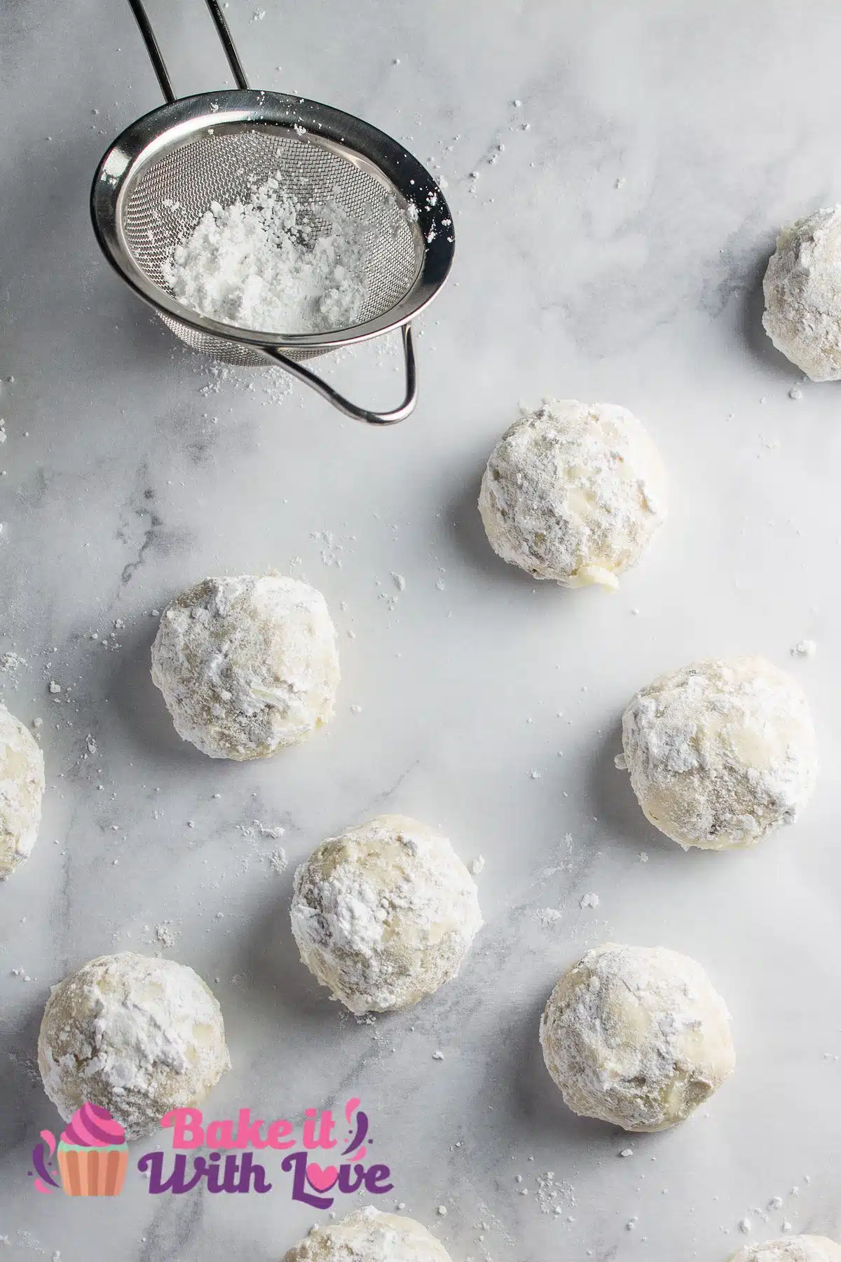 Mexican wedding cookies on parchment paper with a small fine mesh strainer for sprinkling or dusting with more powdered sugar.