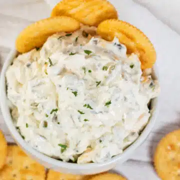 Wide overhead of the olive dip in white serving bowl with buttery crackers around it.