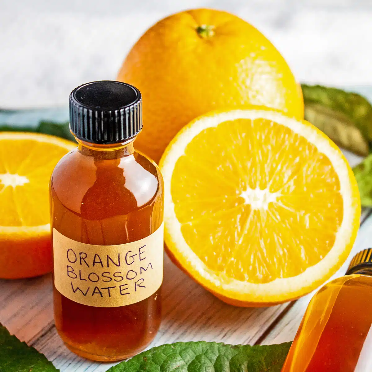 Orange blossom water bottled with sliced oranges and green leaves around it.