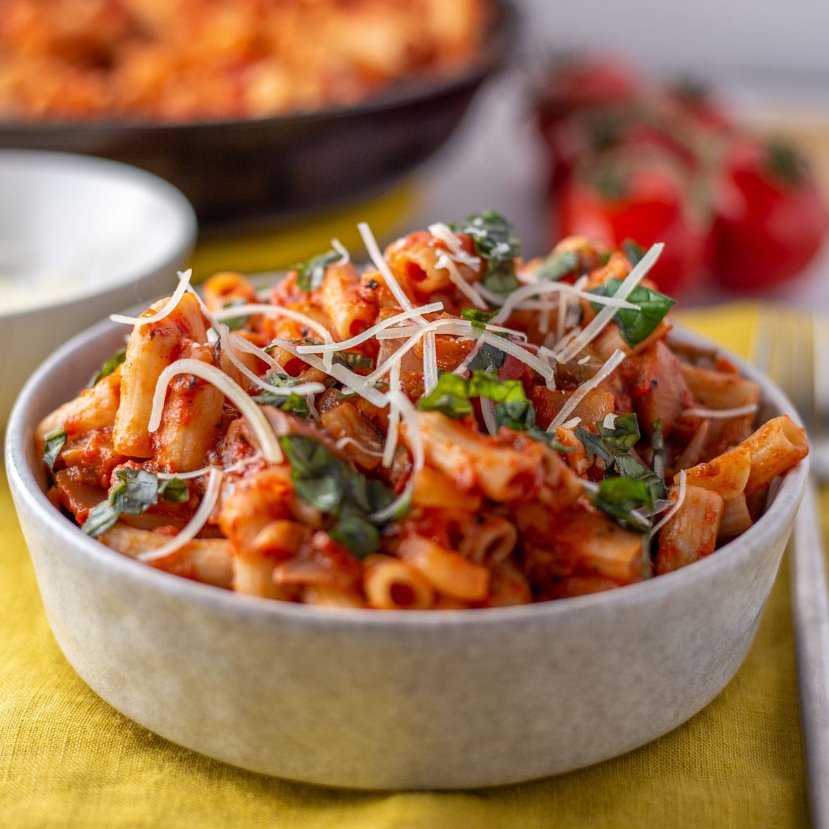 Delicious pasta alla Norma served in an offwhite bowl and garnished with grated Parmesan cheese and chopped basil.