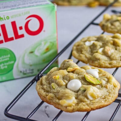 Tasty pistachio pudding cookies on wire cooling rack with boxed instant pistachio pudding mix in the background.