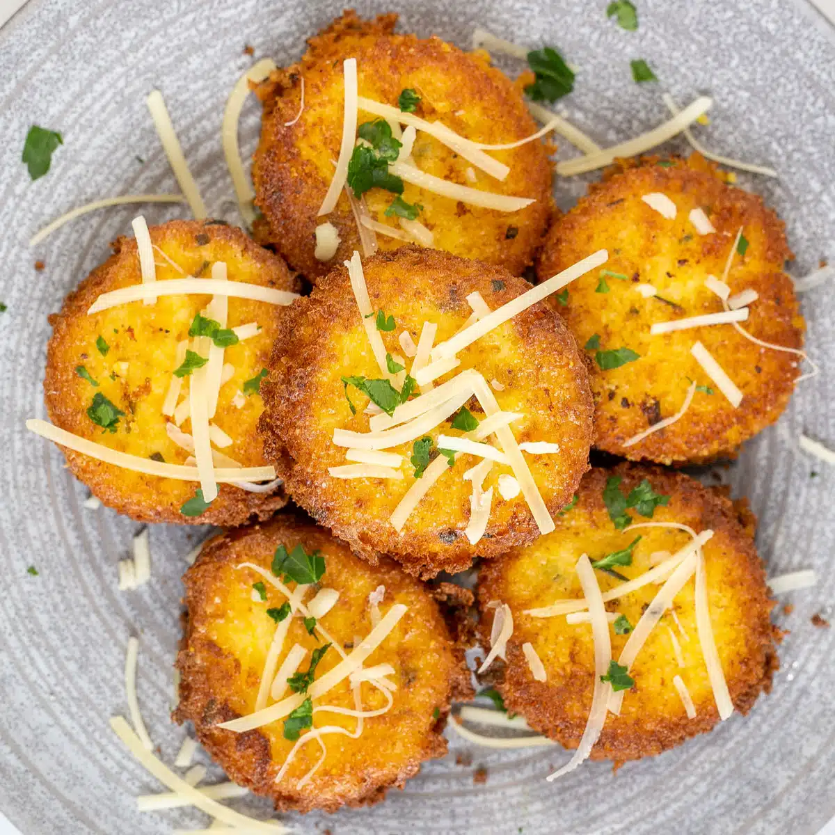 Best polenta cakes served on grey plate with grated parmesan cheese and fresh herbs.