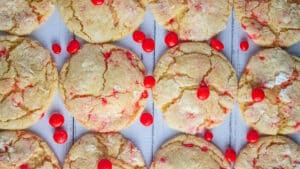 Overhead van de roodgloeiende koekjes op lichte houten achtergrond in rijen met verspreide snoepjes op en rond de koekjes.