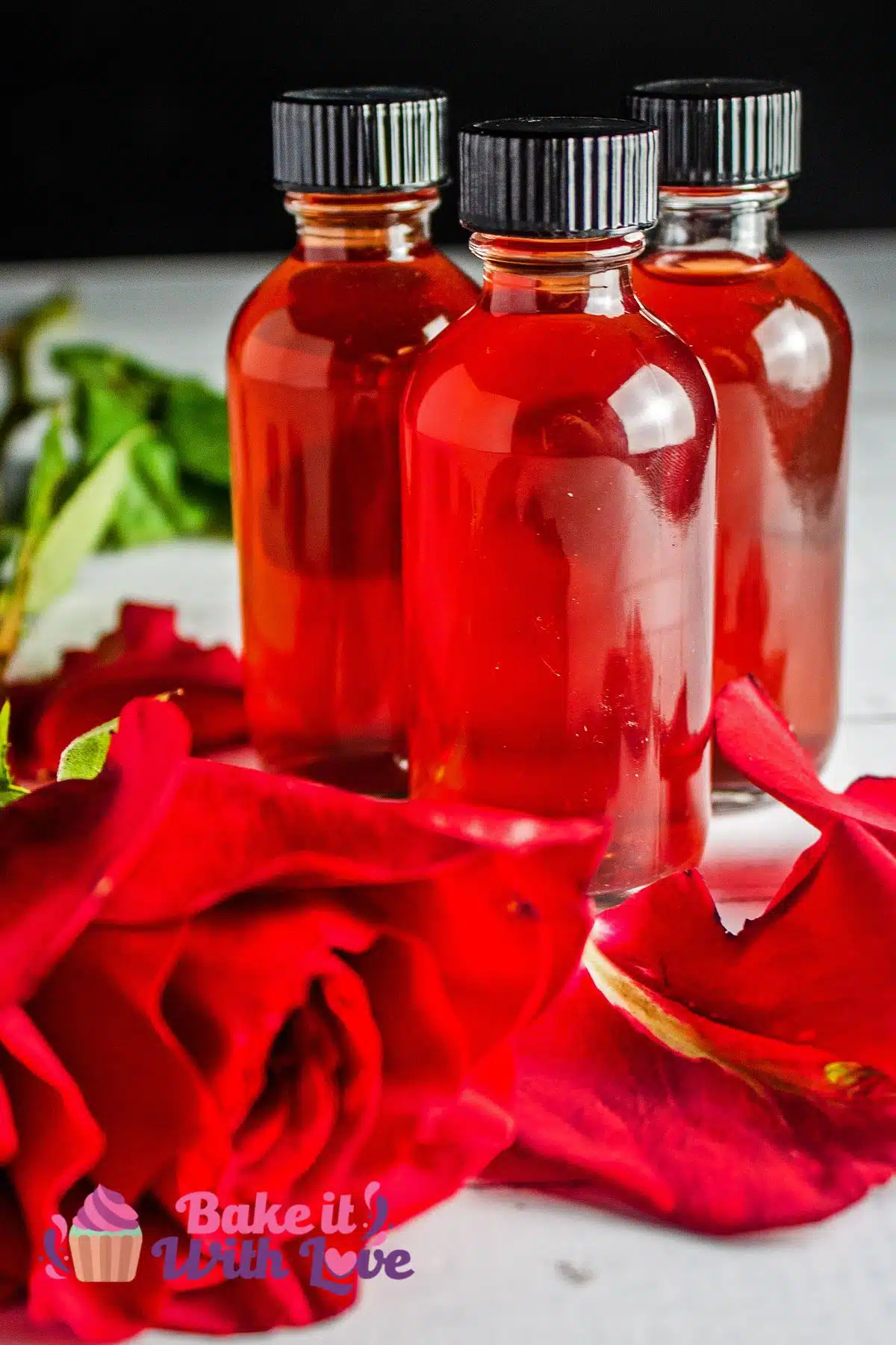 Tall image of three bottles of DIY rose water with roses around them.