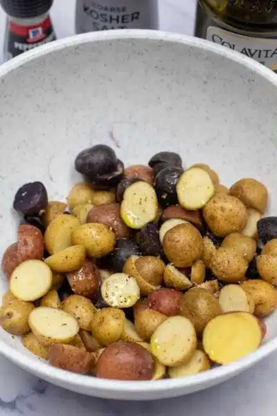 Process image 1 showing baby potatoes sliced in a bowl with olive oil and seasoning.