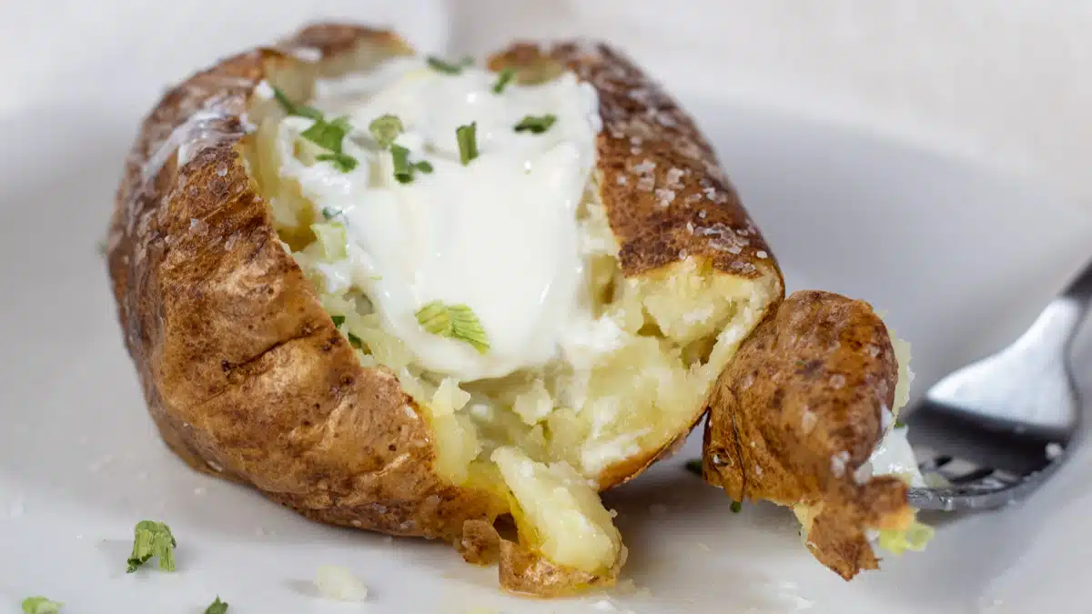 Wide image of air fryer baked potato with sour cream and chives.