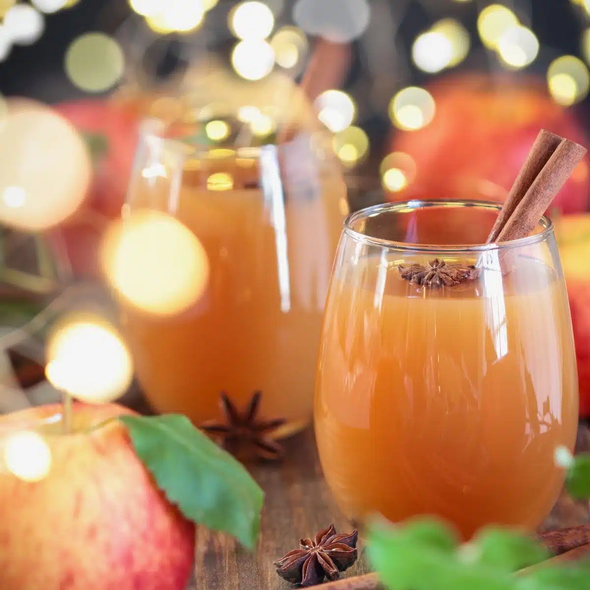 Best apple cider substitute ideas and alternatives to use in any recipe with festive lights behind glasses of apple cider.