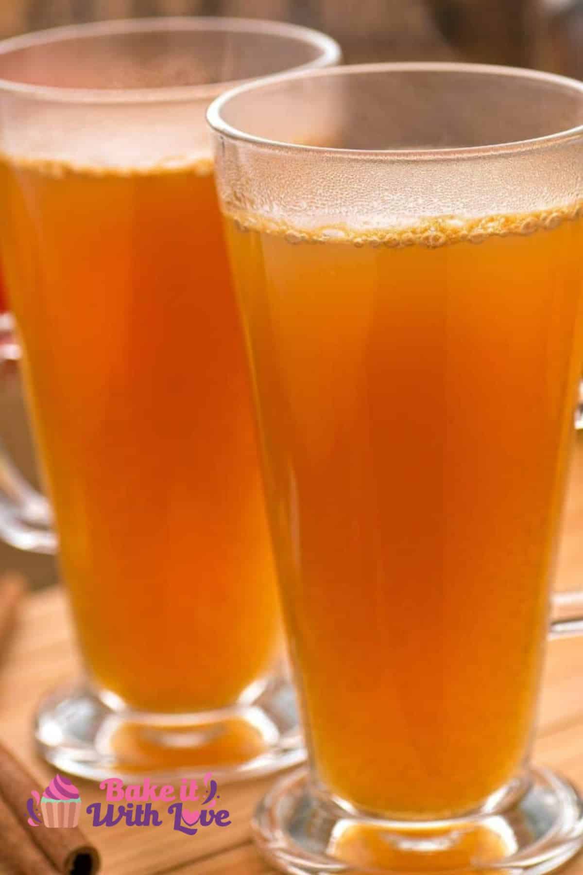 A tall image showing a closeup of two tall pilsner glasses filled with homemade apple cider.