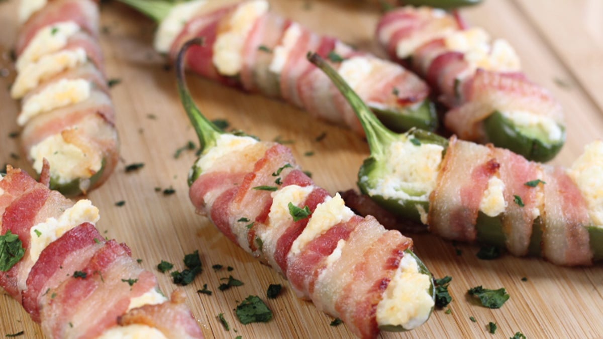 Wide image of bacon wrapped jalapeno poppers with cream cheese.