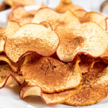 Wide image of a plate of baked cinnamon apple chips.