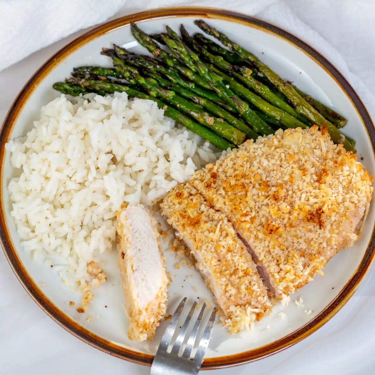 Square image of baked panko chicken on a plate with rice and asparagus.