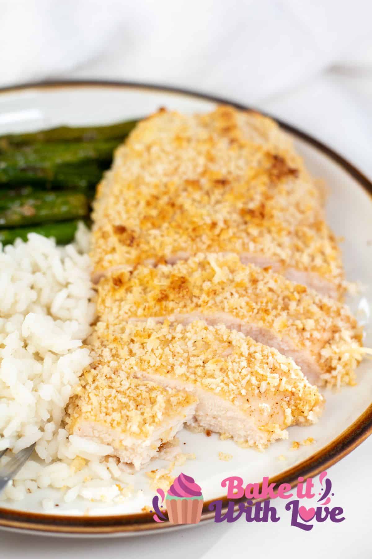 Tall image of baked panko chicken on a plate with rice and asparagus.