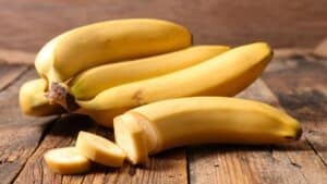Melhor substituto de banana com bananas perfeitamente amarelas em fundo de madeira com a parte da frente cortada parcialmente.