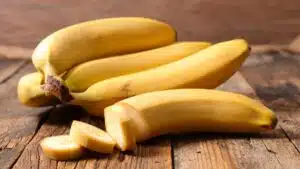 Best banana substitute featuring perfectly yellow bananas on wooden background with the front one sliced partially.