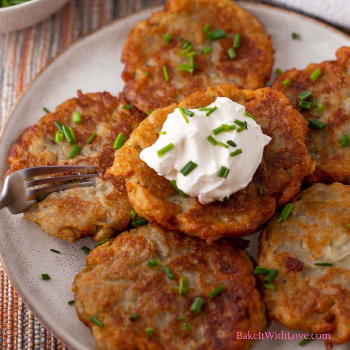 Square image of boxty Irish pancakes on a plate with sour cream being cut with a fork.