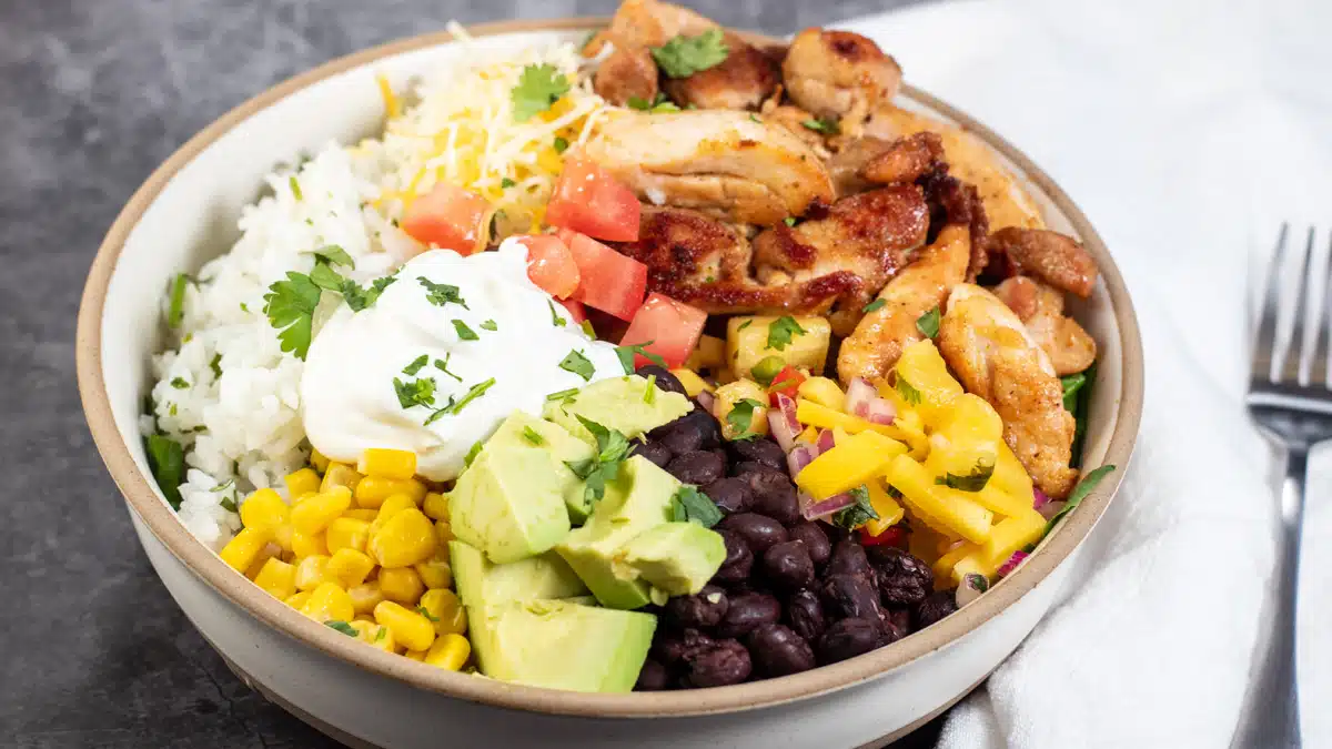Best easy chicken burrito bowl recipe to assemble with tasty toppings like corn, black beans, salsa, diced tomatoes and avocados on top of a bed of lettuce and cilantro lime rice.