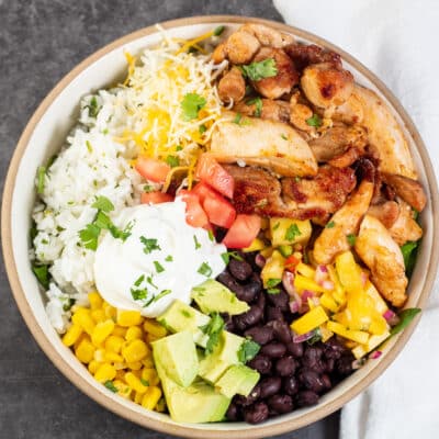 Best chicken burrito bowl recipe with cilantro lime rice, beans, sweet corn, diced avocado, mango salsa, and more.