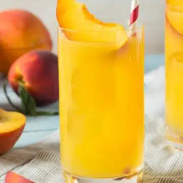 Wide angle image of a fuzzy navel cocktail with a peach slice and straw.
