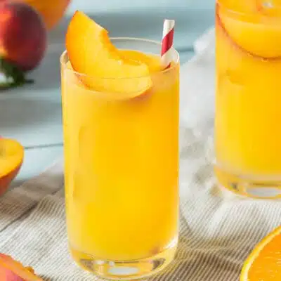 Square image of a fuzzy navel cocktail with a peach slice and straw.