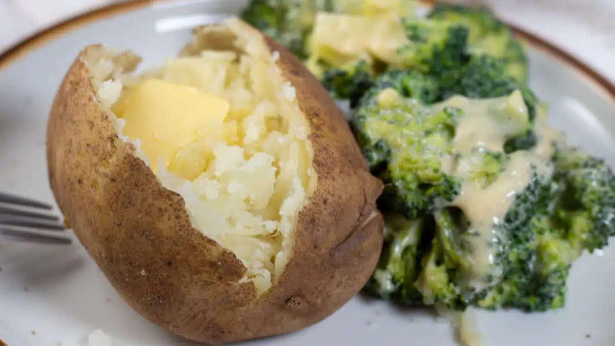 Wide image showing a plate with a instant pot baked potato and broccoli on the side.
