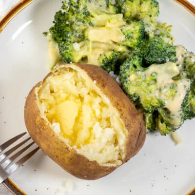 Vierkante afbeelding van een bord met een kant-en-klare aardappel in de stoofpot en broccoli aan de zijkant.