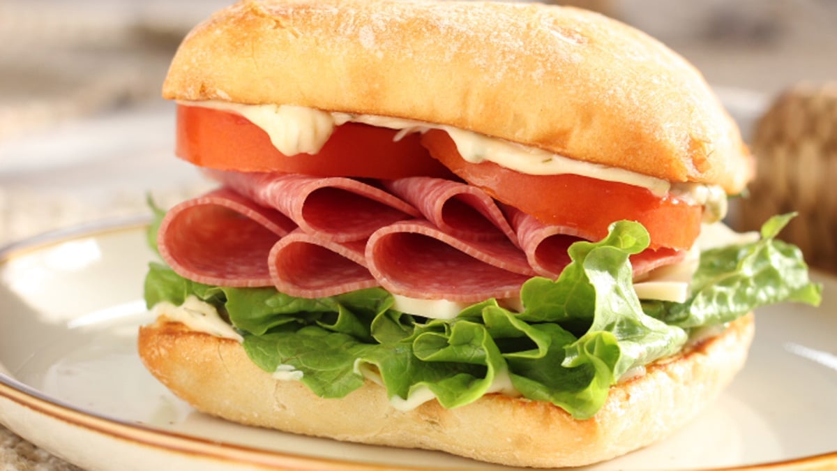 Wide image of a salami sandwich on a white plate.